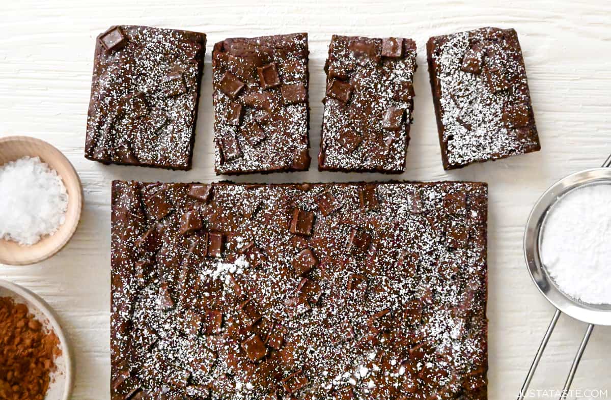 Fudgy homemade brownies dusted with powdered sugar next to a sifter containing powdered sugar.