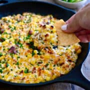 A hand dips a tortilla chip into easy corn dip in a cast iron skillet.