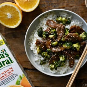 A top down view of Orange Beef and Broccoli in a bowl with chopsticks and sliced oranges next to it