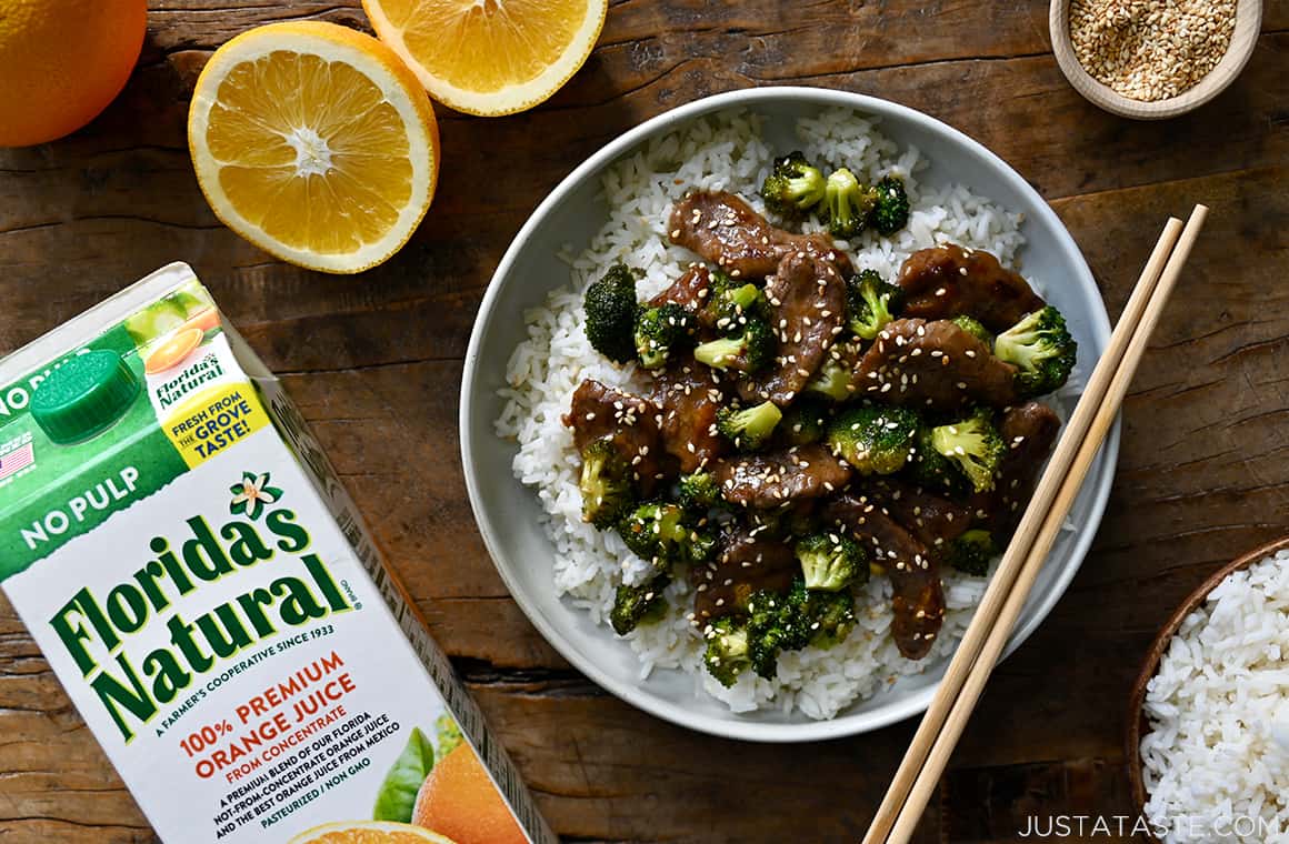 A top down view of Orange Beef and Broccoli in a bowl with chopsticks and sliced oranges next to it