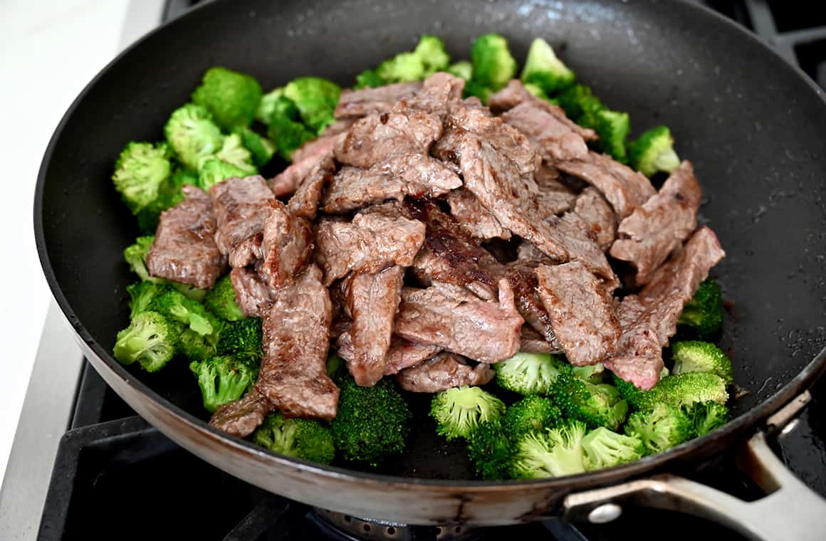 A skillet on a stovetop containing beef and broccoli