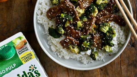A top down view of a plate containing rice, beef and broccoli with oranges next to it