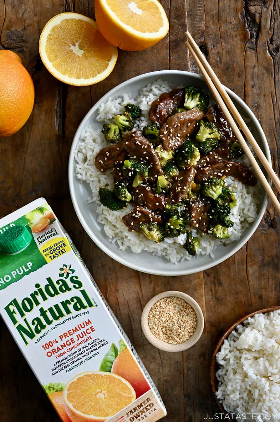 A top down view of a plate containing rice, beef and broccoli with oranges next to it