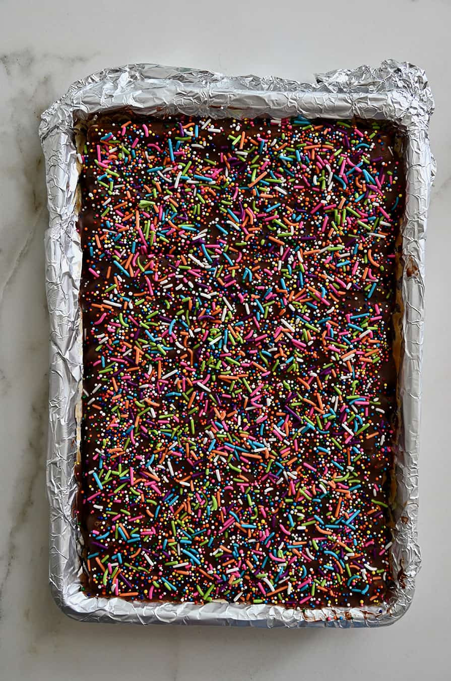 A foil-lined baking sheet containing pretzel bark topped with chocolate and sprinkles
