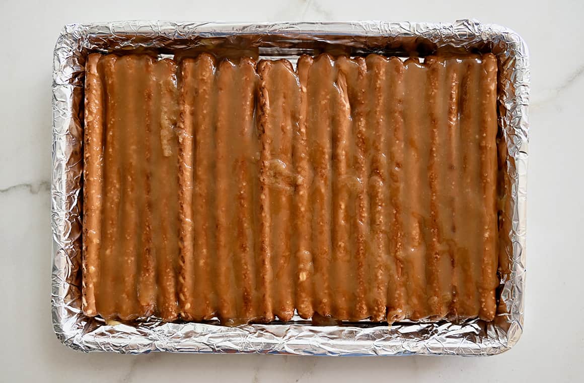 Una teglia foderata di alluminio contenente bastoncini di pretzel ricoperti di caramello