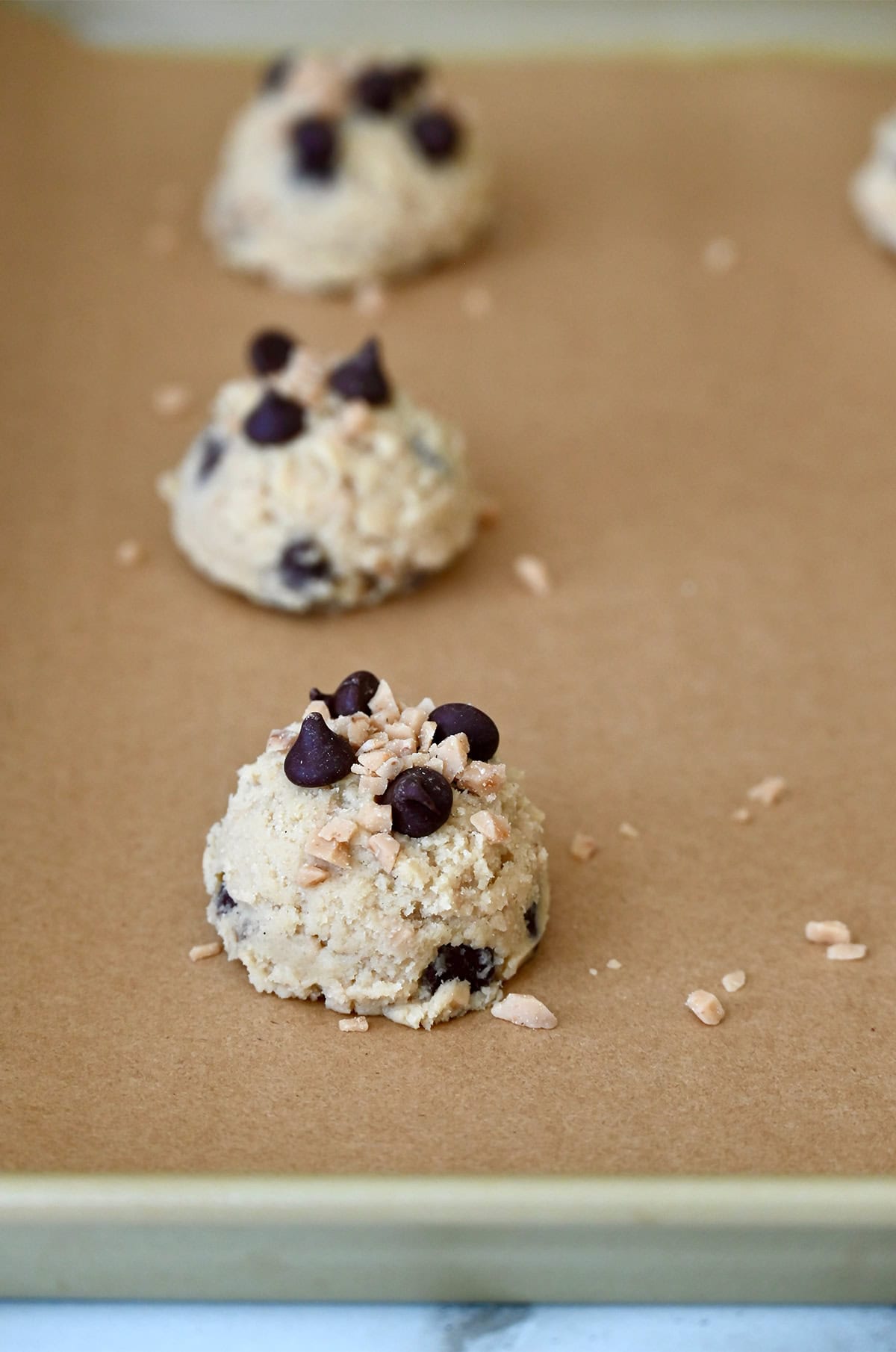 Balls of cookie dough topped with chocolate chips on a baking sheet lined with parchment paper.