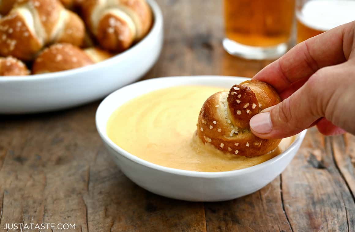 A soft pretzel knot being dunked in a bowl of beer cheese sauce