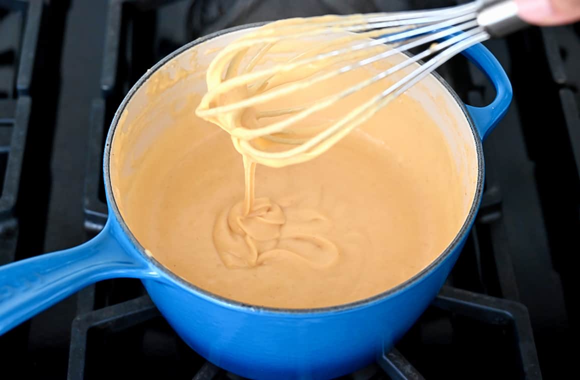 A blue saucepot containing melted cheese with a whisk
