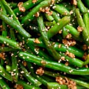 A close-up view of blistered garlic green beans garnished with toasted sesame seeds.