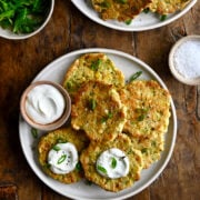 A top-down view of two plates containing corn and zucchini fritters topped with sour cream and chopped scallions.