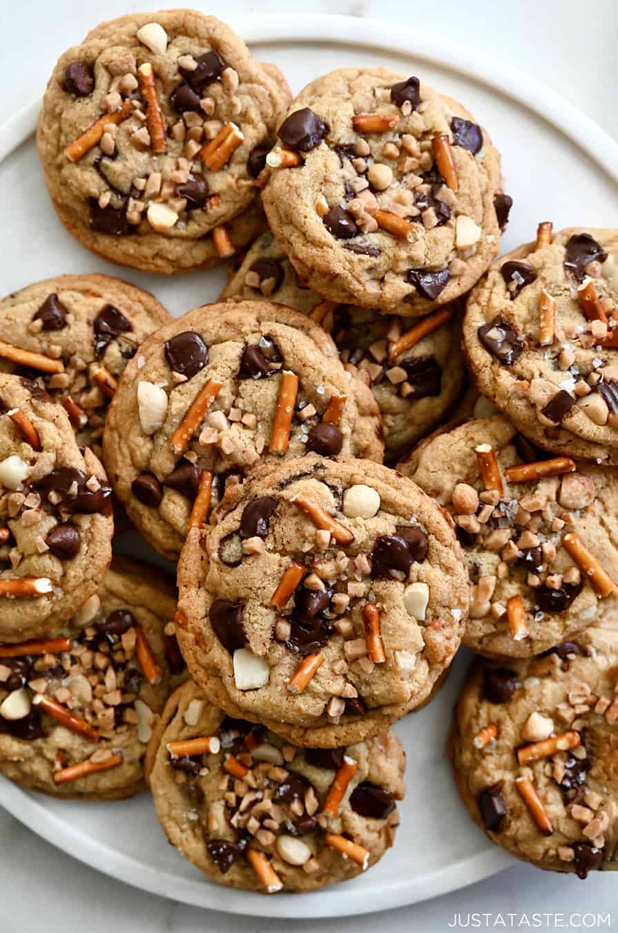 A top-down view of soft and chewy Kitchen Sink Cookies studded with crushed pretzels, chocolate chunks and chopped macadamia nuts on a white plate