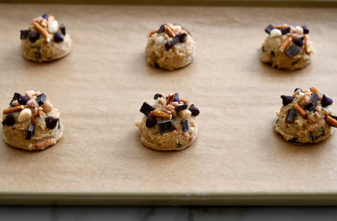 Scoops of dough topped with chocolate chunks on a parchment paper-lined baking sheet