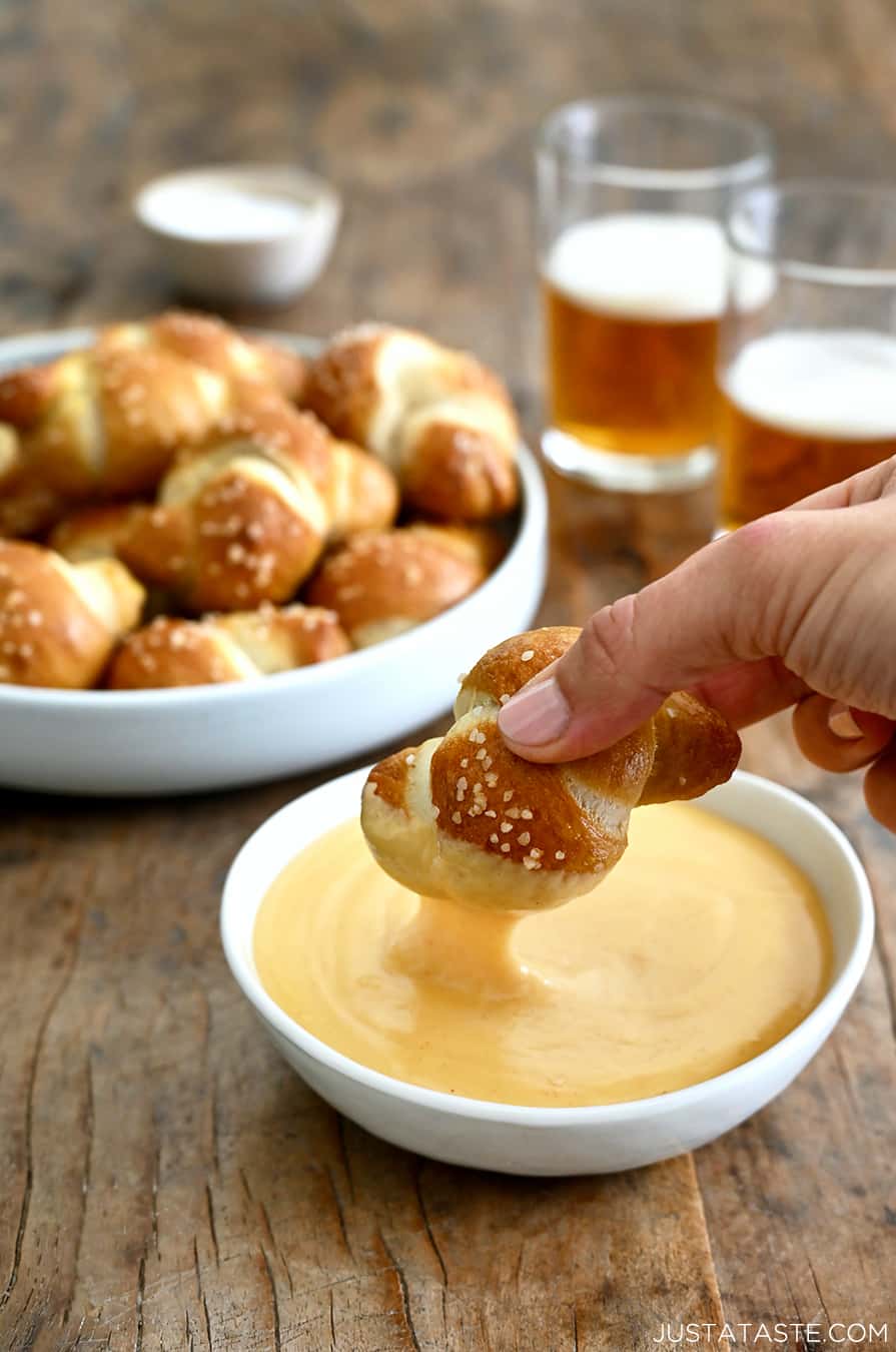 A soft pretzel knot being dipped into a bowl of beer cheese sauce