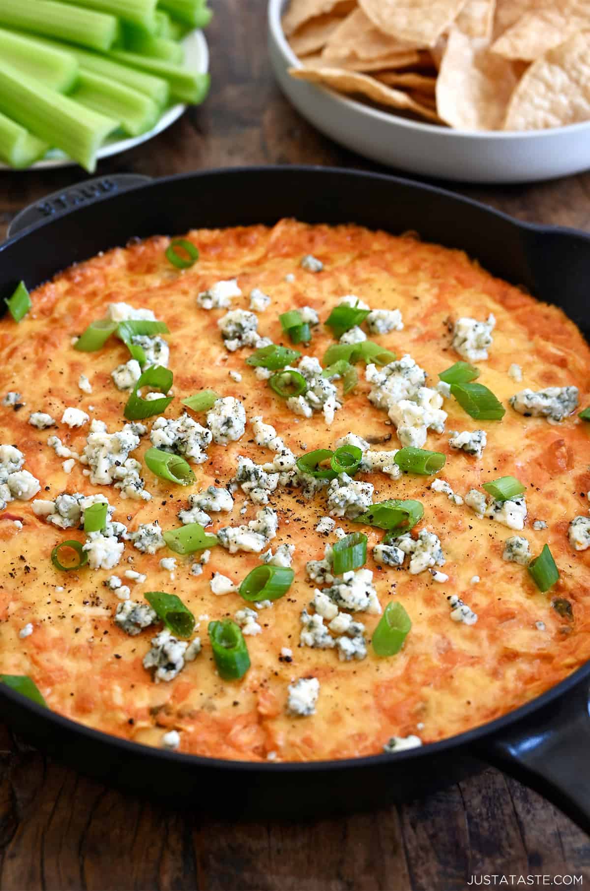 Buffalo chicken dip in a skillet topped with blue cheese crumbles and sliced green onions.