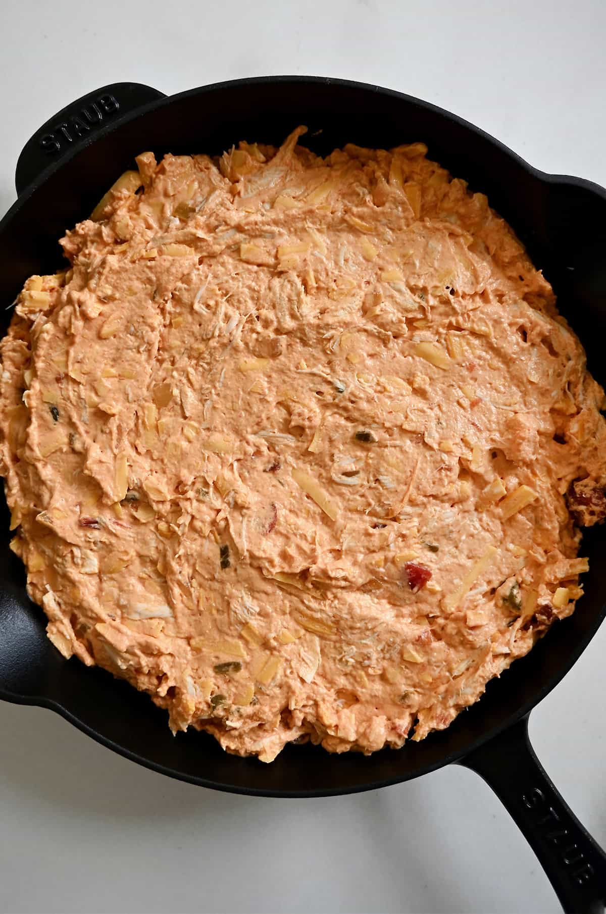 Buffalo chicken dip spread evenly in a cast-iron skillet before baking.