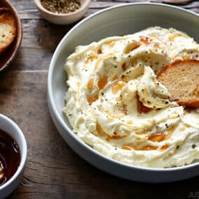 A bowl of whipped Brie cheese with a toast and a bowl of honey next to it