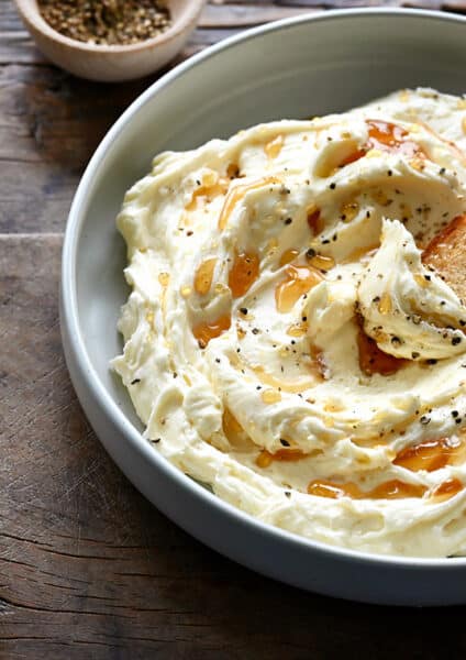 A bowl of whipped Brie cheese with a toast and a bowl of honey next to it
