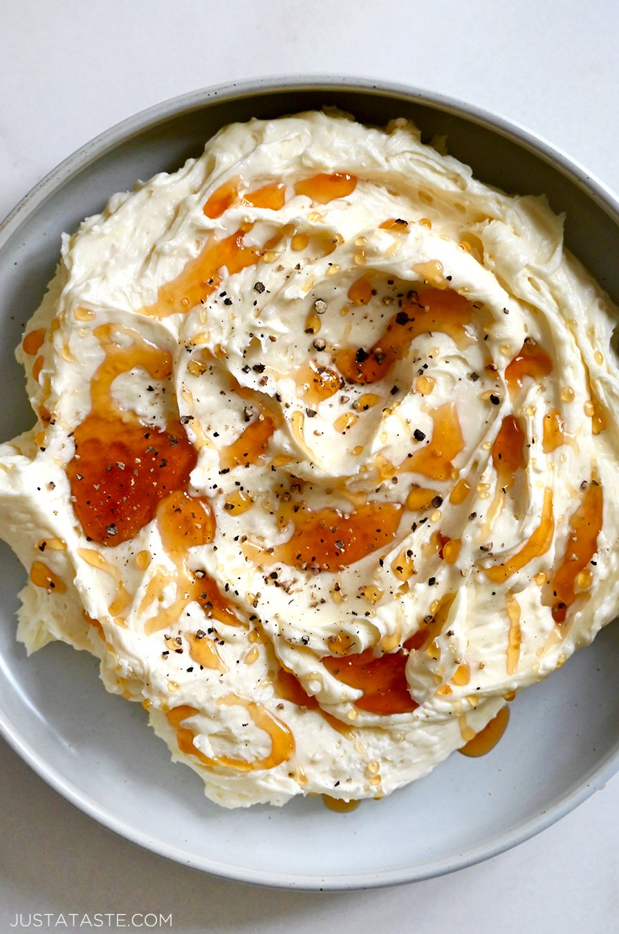 A top-down close-up view of a grey bowl containing whipped Brie cheese topped with honey and black pepper