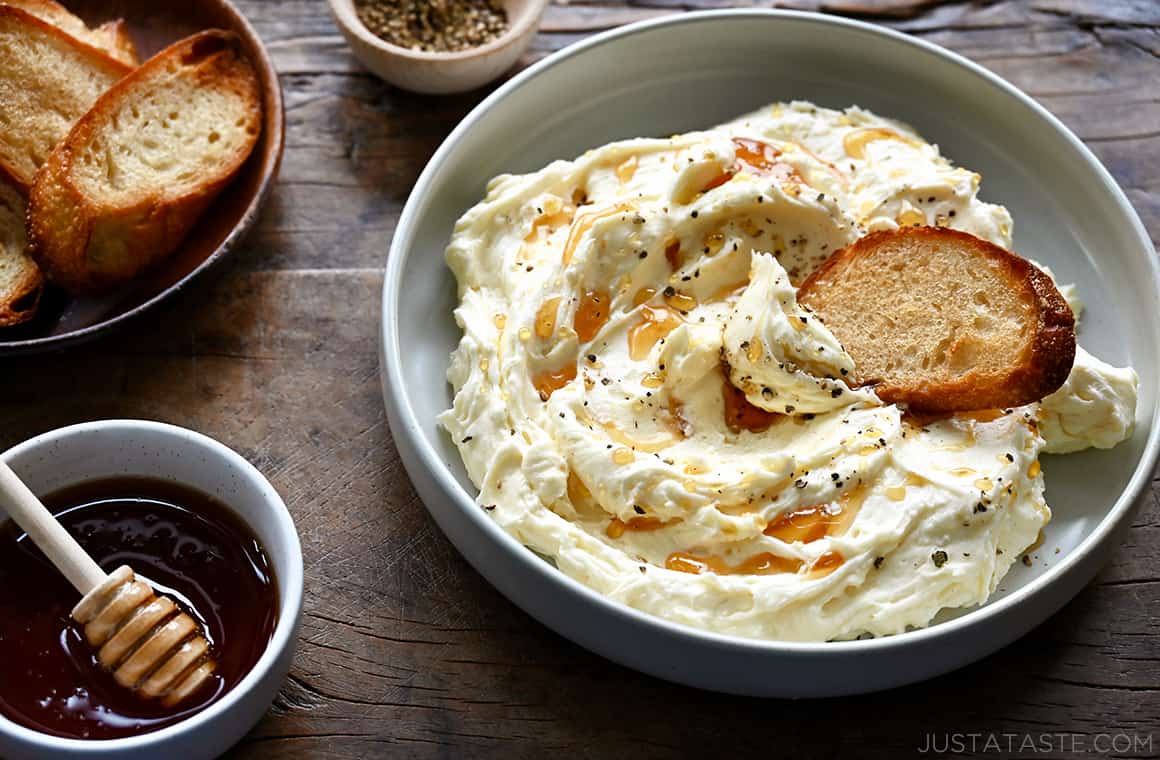 A bowl of whipped Brie cheese with a toast and a bowl of honey next to it