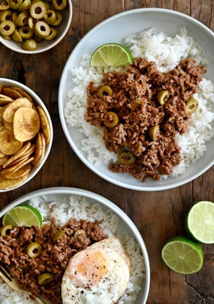Two plates containing white rice topped with Cuban Picadillo and a fried egg.