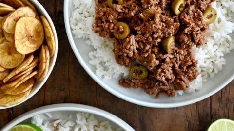 Two plates containing white rice topped with Cuban Picadillo and a fried egg.