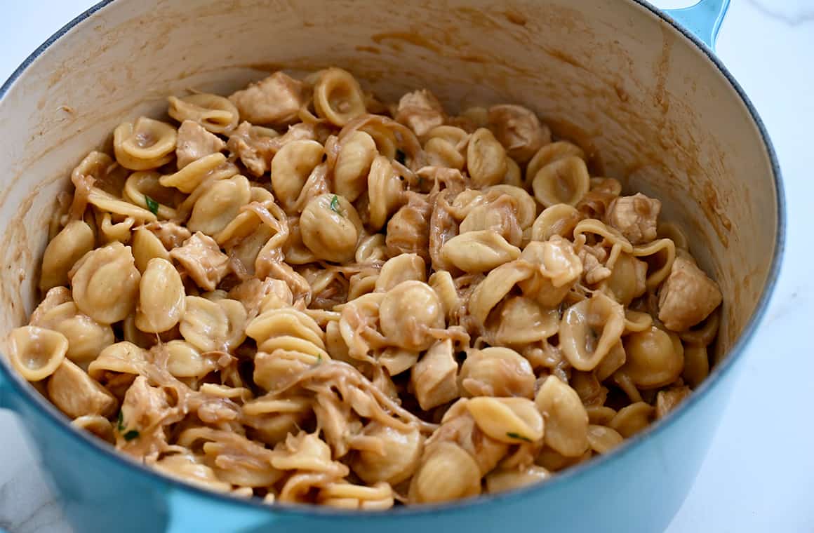 A stockpot containing cooked pasta in a oniony sauce