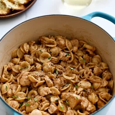 A blue stockpot containing French onion orecchiette pasta with chicken next to a plate topped with cheesy baguette toasts