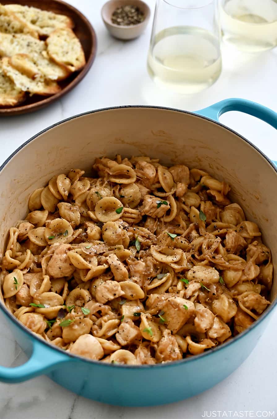 A blue stockpot containing French onion orecchiette pasta with chicken next to a plate topped with cheesy baguette toasts