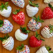 A top-down view of white chocolate-covered strawberries - some decorated with rainbow sprinkles, others with red sanding sugar.