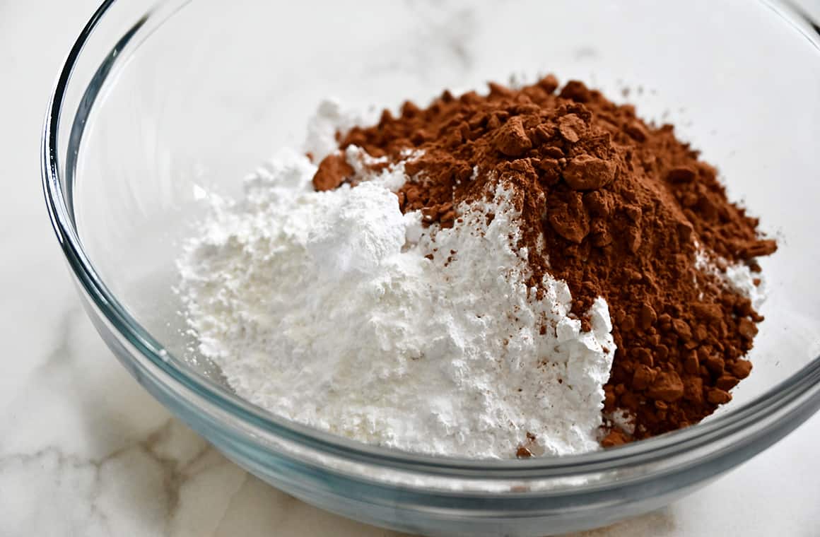 A clear bowl containing cocoa powder and powdered sugar
