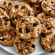 Kitchen sink cookies studded with crushed pretzels, chocolate chips, nuts and toffee bits piled on a plate.