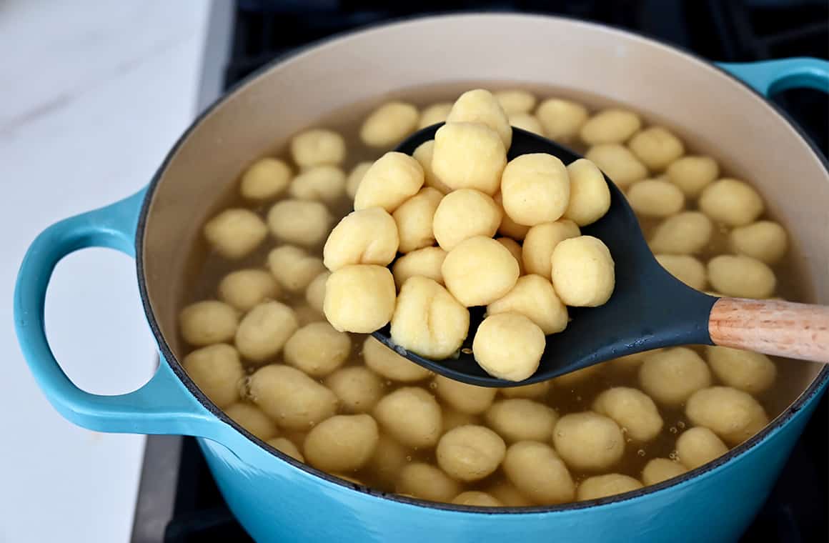 Boiled gnocchi in a spoon over a large stockpot with water and gnocchi.