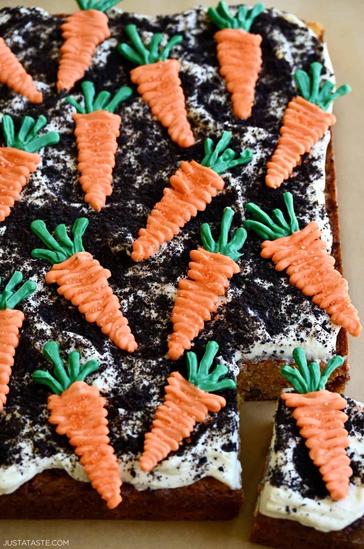 Carrot sheet cake topped with cream cheese frosting, crushed chocolate cookies and candy melt carrots.