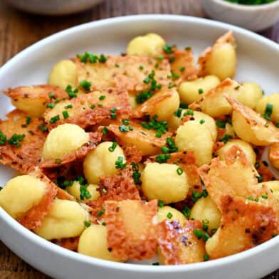 Crispy parmesan gnocchi garnished with chopped fresh chives piled high in a bowl.