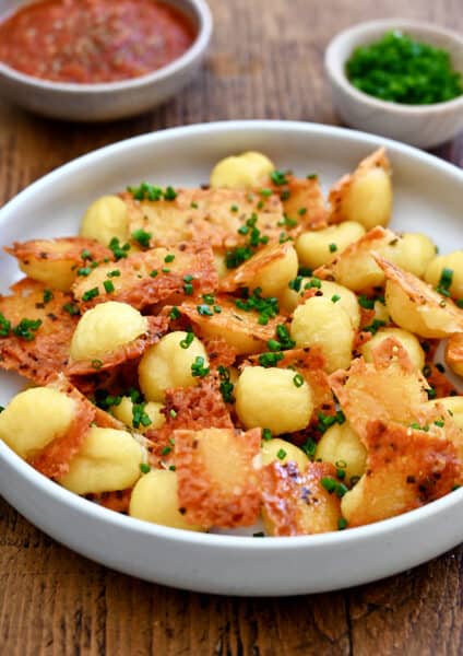 Crispy parmesan gnocchi garnished with chopped fresh chives piled high in a bowl.