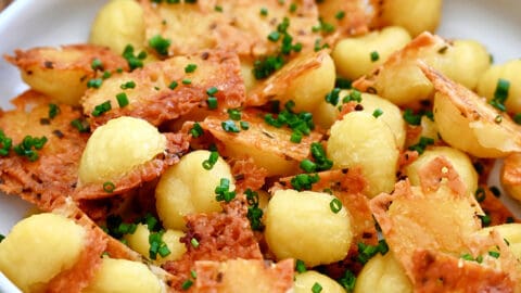 Crispy parmesan gnocchi garnished with chopped fresh chives piled high in a bowl.