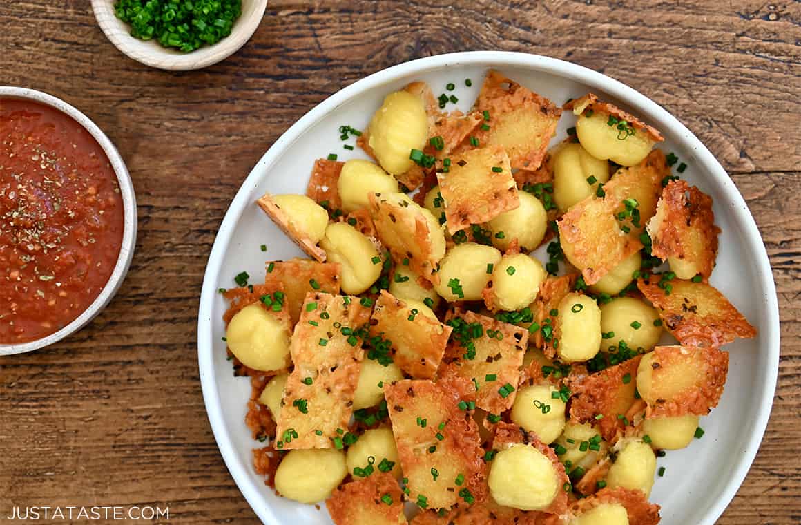 A top-down view of gnocchi with a crispy parmesan bottom on a plate next to a small bowl filled with marinara sauce.