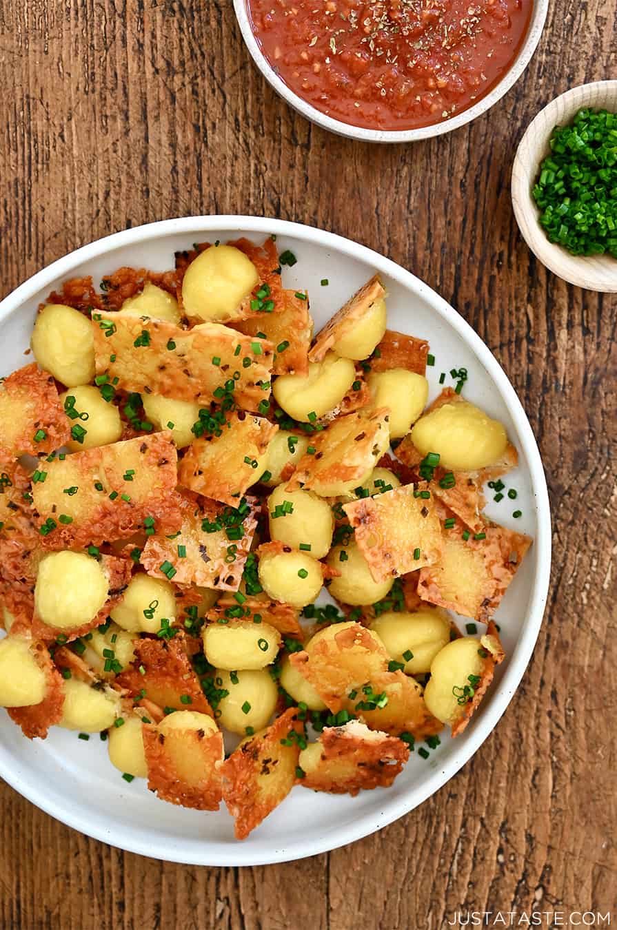 A top-down view of crispy potato dumplings with cheesy bottoms on a plate and garnished with fresh chives.