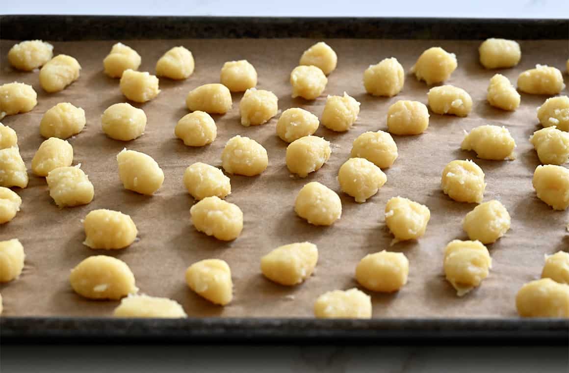 Cooked gnocchi cooling on a parchment paper-lined baking sheet.