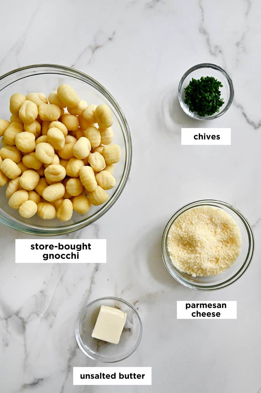 A top-down view of three various sizes of bowls containing store-bought gnocchi, chopped chives, grated parmesan and unsalted butter.