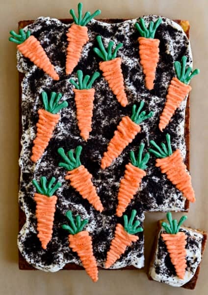 A 9x13 carrot sheet cake topped with crushed chocolate cookie "dirt" and orange candy melt carrots "planted" in the cream cheese frosting.