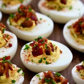 A close-up view of The Best Deviled Eggs with Bacon garnished with fresh chives and paprika.