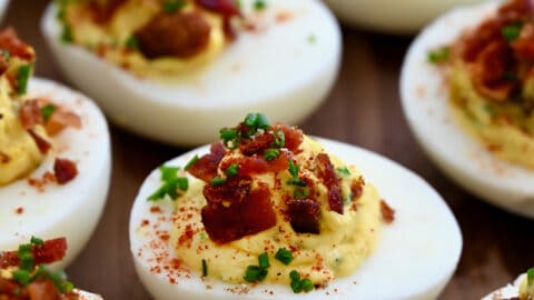 A close-up view of The Best Deviled Eggs with Bacon garnished with fresh chives and paprika.