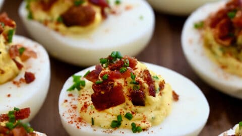 A close-up view of The Best Deviled Eggs with Bacon garnished with fresh chives and paprika.