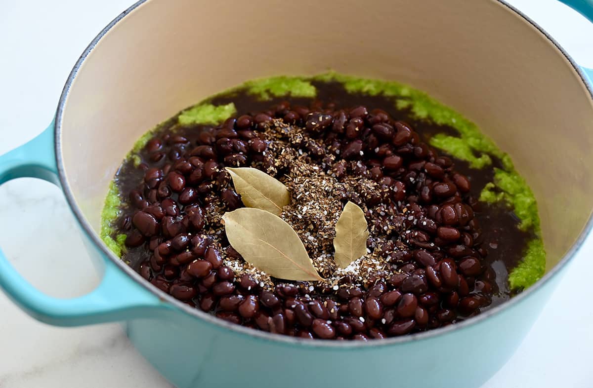 A large pot containing sofrito, black beans, oregano, and bay leaves.