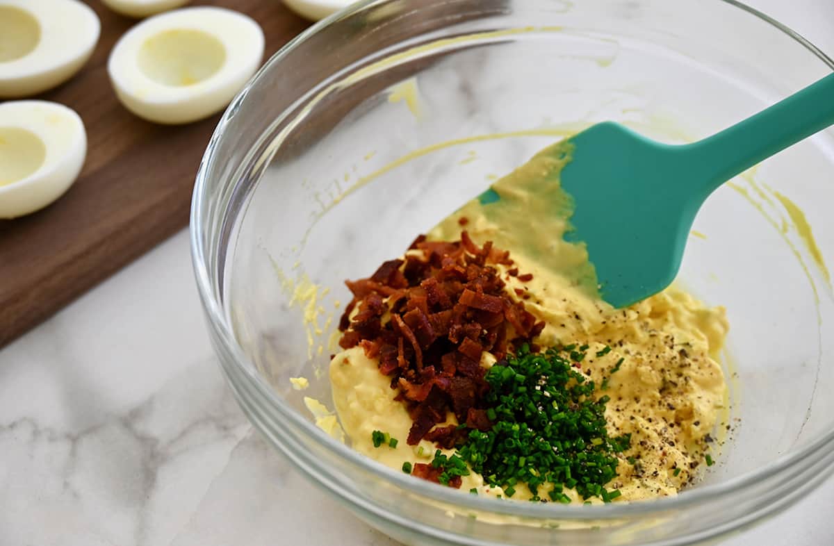 A clear bowl containing mashed yolks with chopped fresh chives and crumbled bacon.
