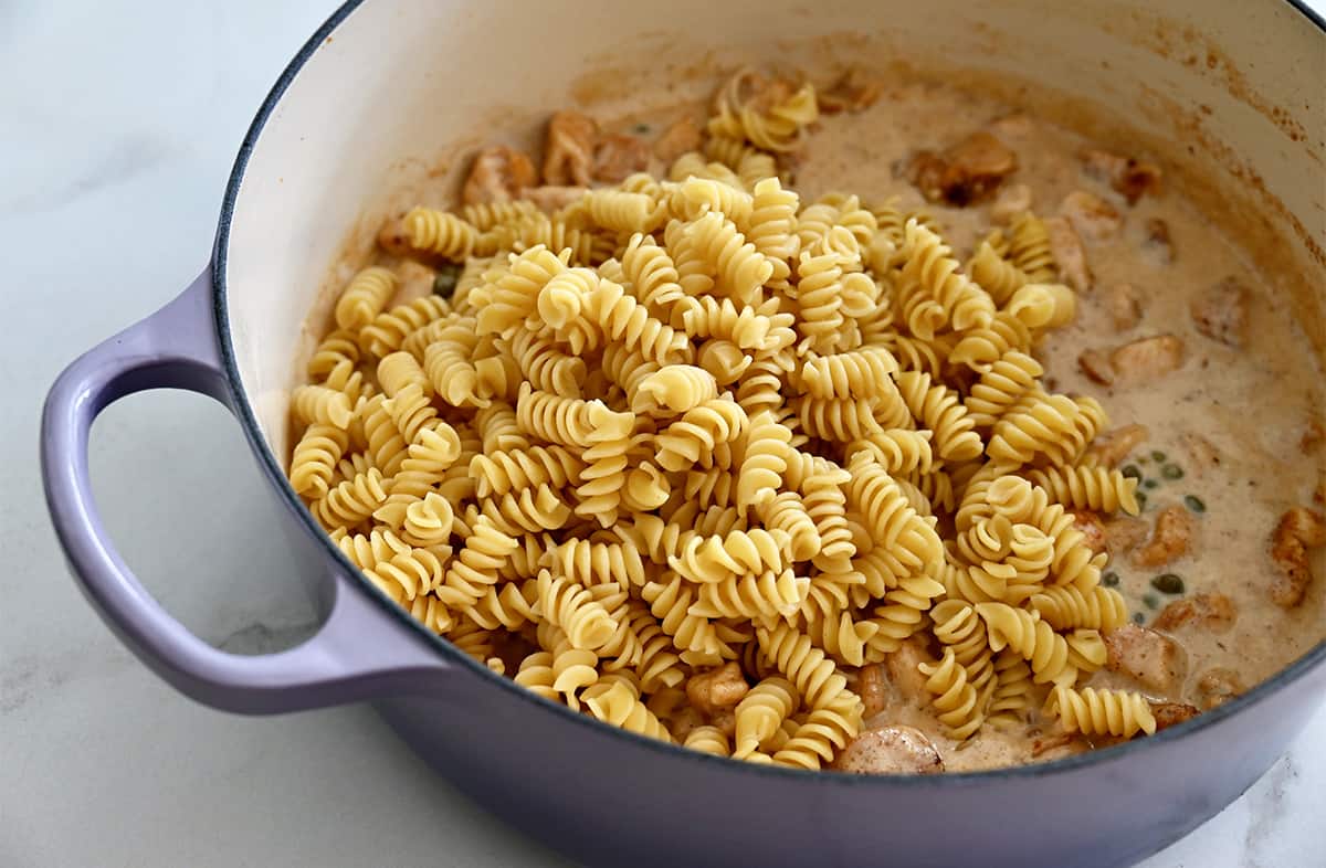 Uncooked pasta over a creamy sauce in a large saucepan.