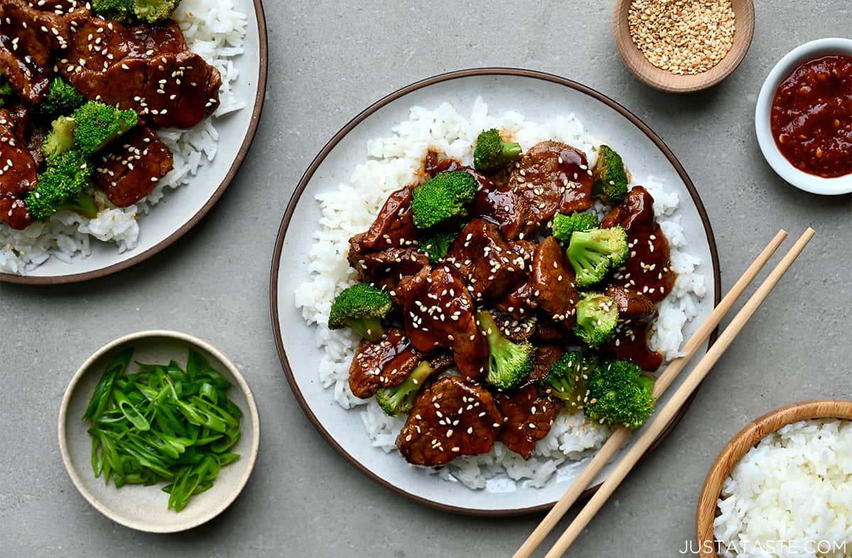 A top-down view of chopsticks resting on a plate containing caramelized pork and broccoli over white rice.
