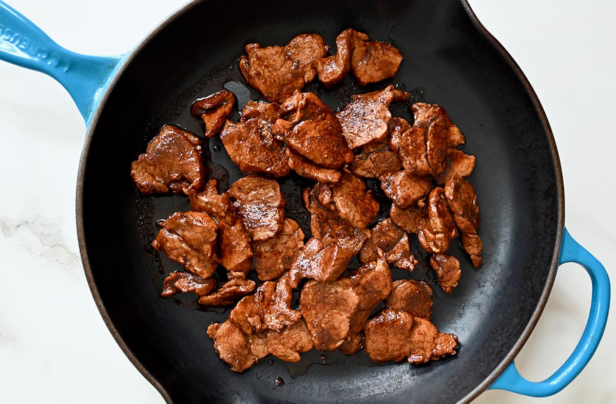 A top-down view of caramelized pork pieces in a large skillet.