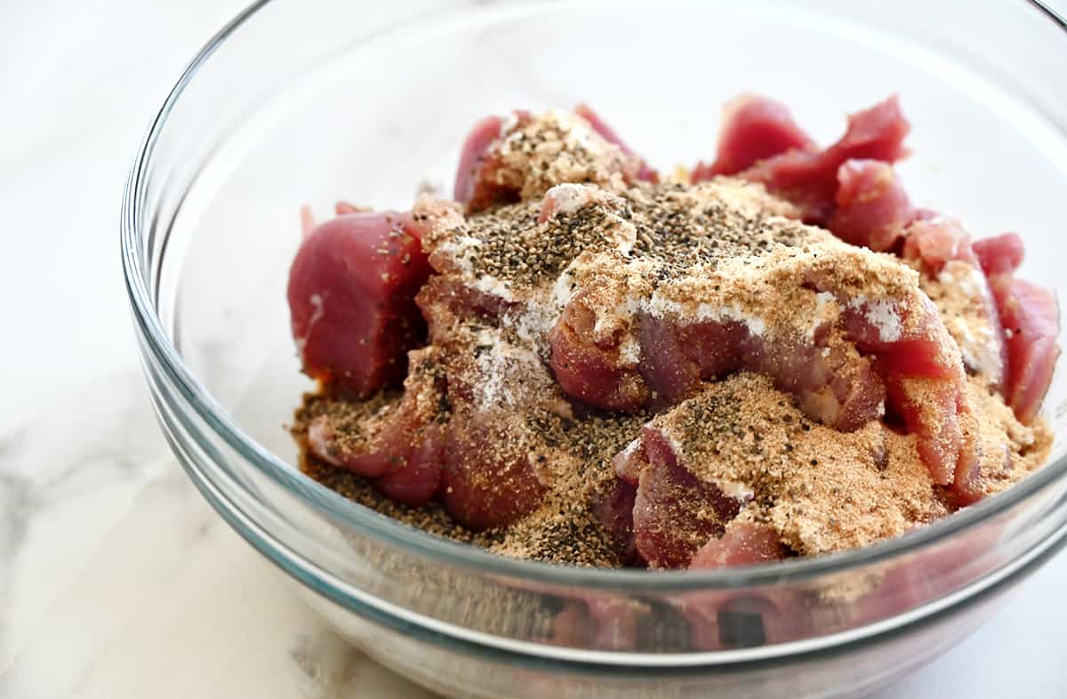 Slices of pork tenderloin in a clear bowl topped with a marinade.